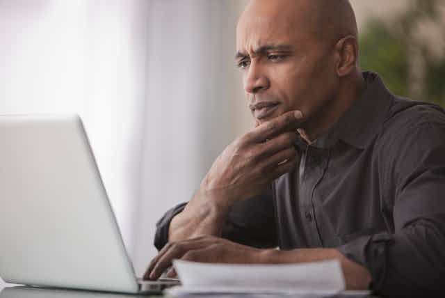 A man with a skeptical expression looks at a laptop