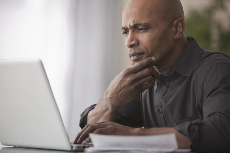 A man with a skeptical expression looks at a laptop