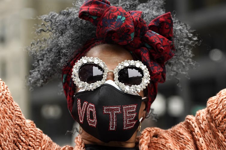 A Black woman wears a face mask embroidered with the word vote.