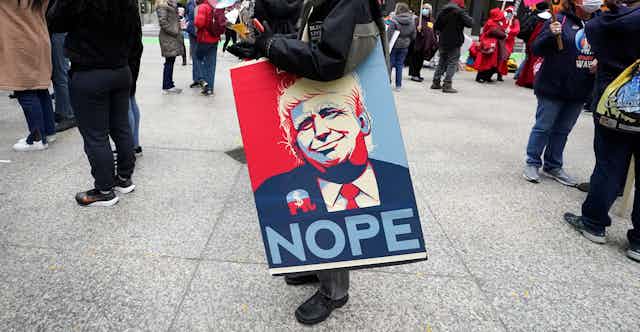 A protester carries a sign featuring Donald Trump and the word 'nope'.