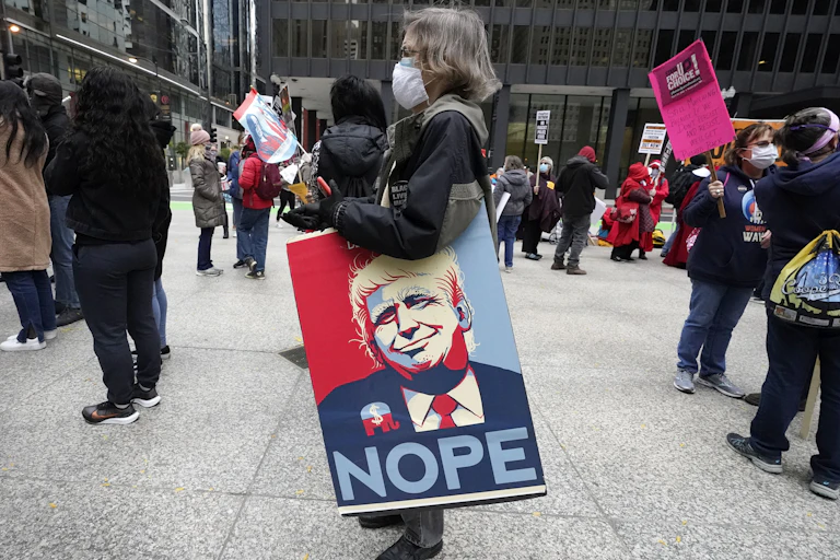 A protester carries a sign featuring Donald Trump and the word 'nope'.