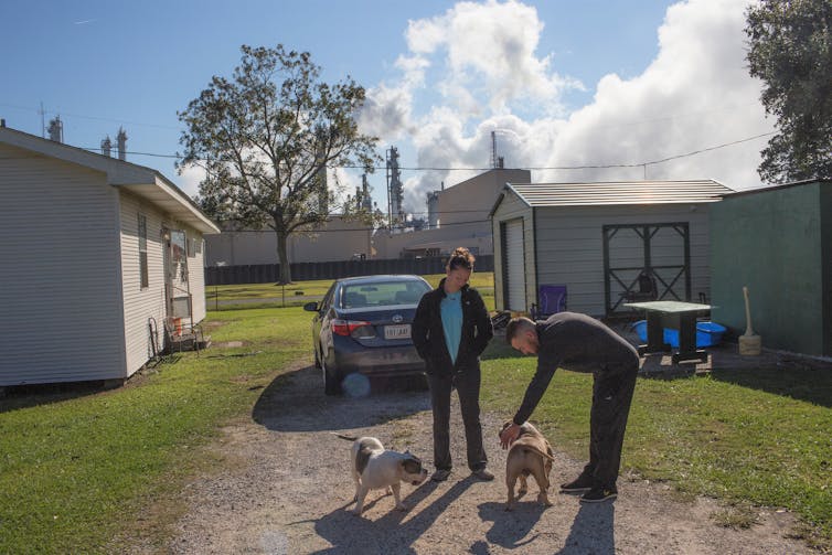 A couple plays with their dogs at a Louisiana home with a refinery in the background.
