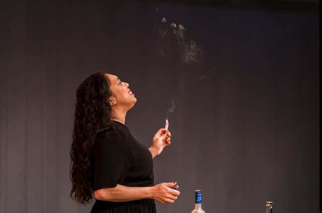 A woman smokes on stage