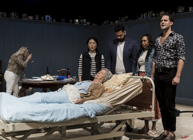 Production photo: the family gather around Nan in a hospital bed