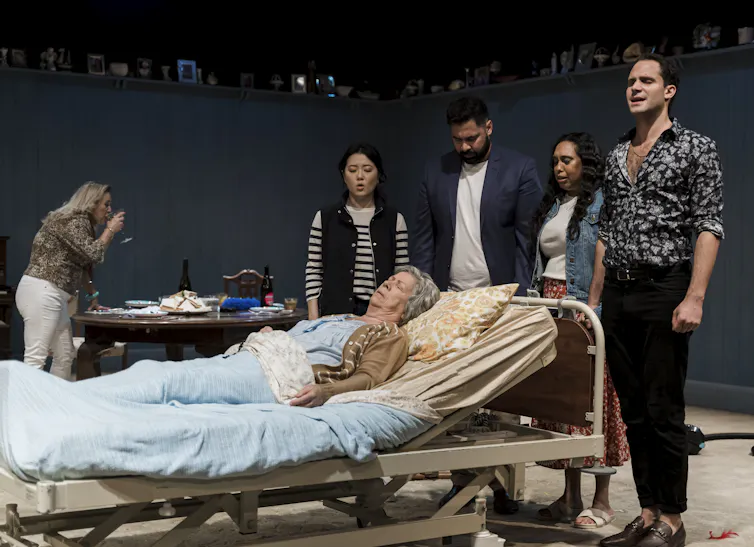 Production photo: the family gather around Nan in a hospital bed