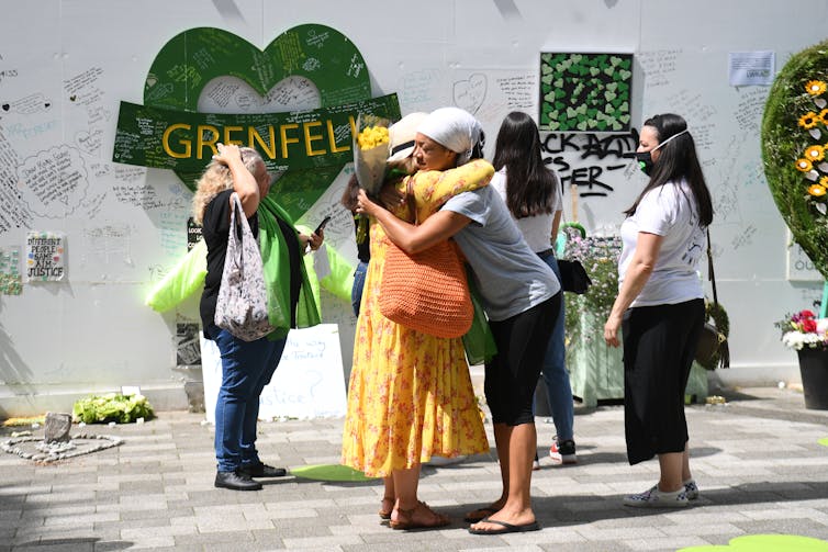 Women hug and look at wall of tributes left for Grenfell victims.