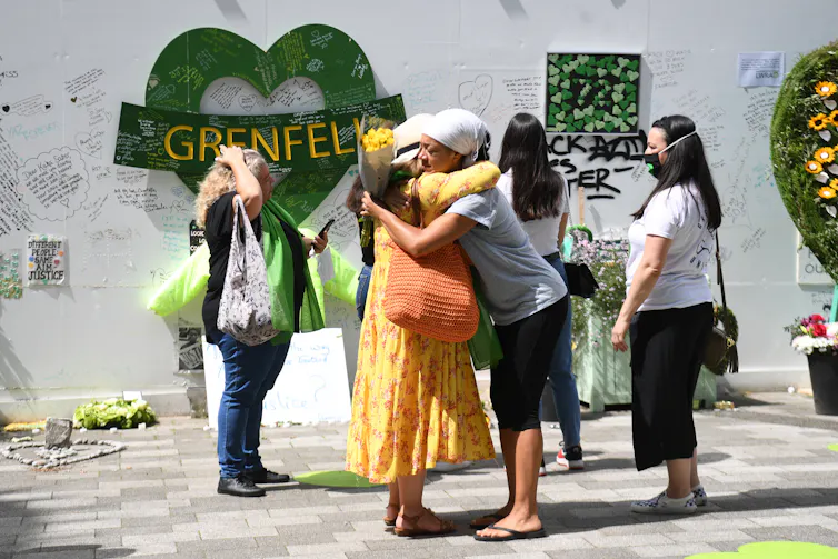 Women hug and look at wall of tributes left for Grenfell victims.