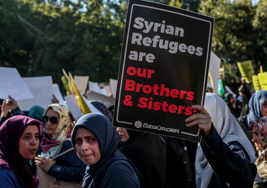Women protesting holding a sign saying 'Syrian Refugees are our brothers and sisters'