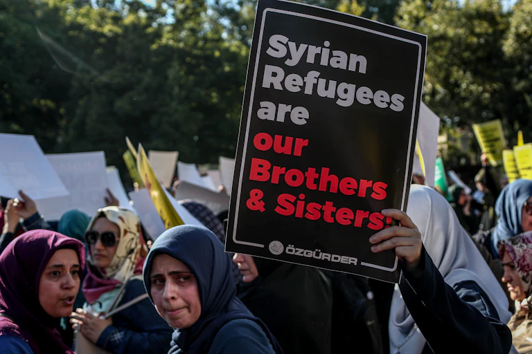 Women protesting holding a sign saying 'Syrian Refugees are our brothers and sisters'