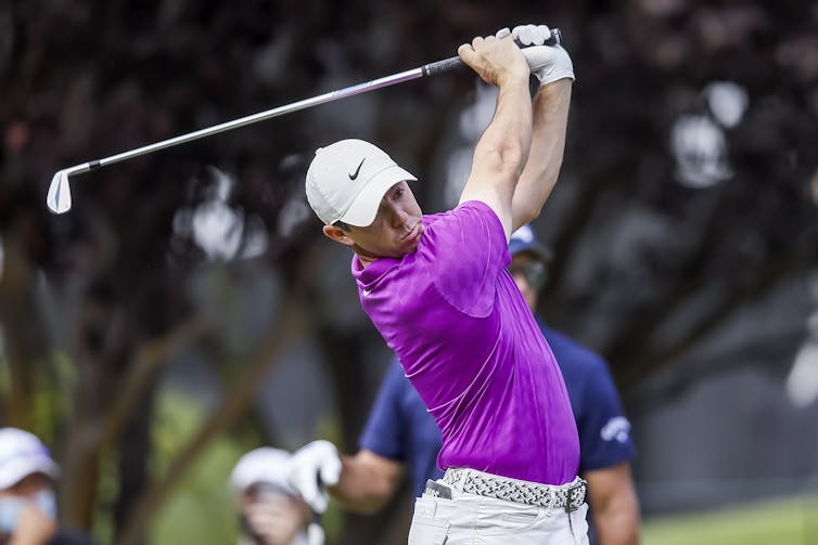 Man in purple shirt swinging golf club