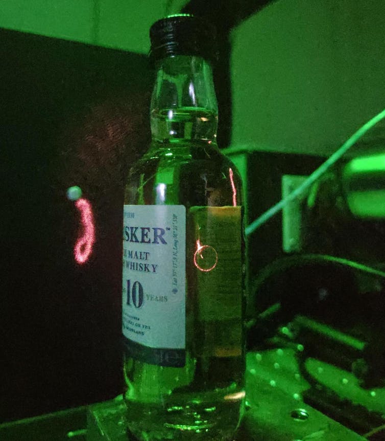 A bottle of whisky with a cone-shaped laser shining through it.