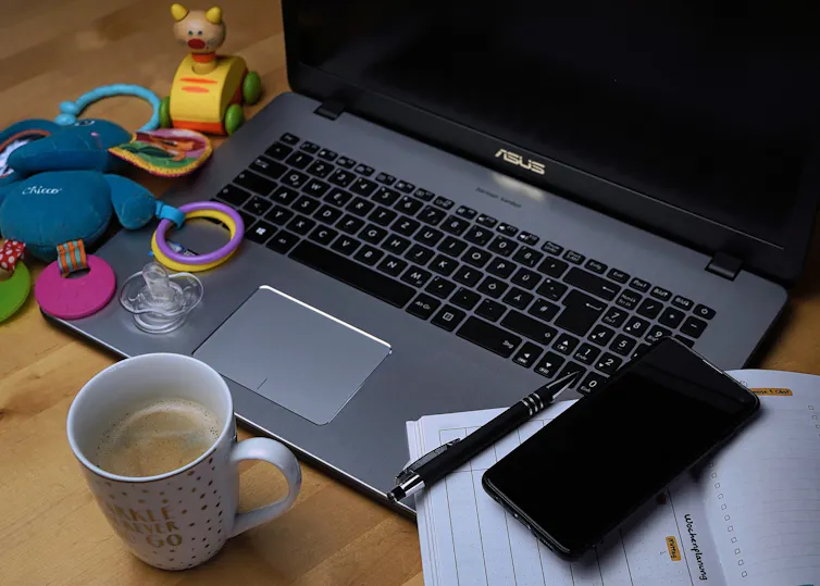 A laptop is seen baby paraphernalia nearby, including a pacifier and teething ring.