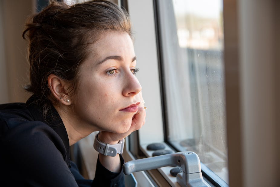 A woman resting her chin on her hand, looking out of a window.
