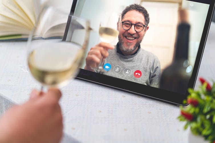 A man on a video screen raising a glass of wine.