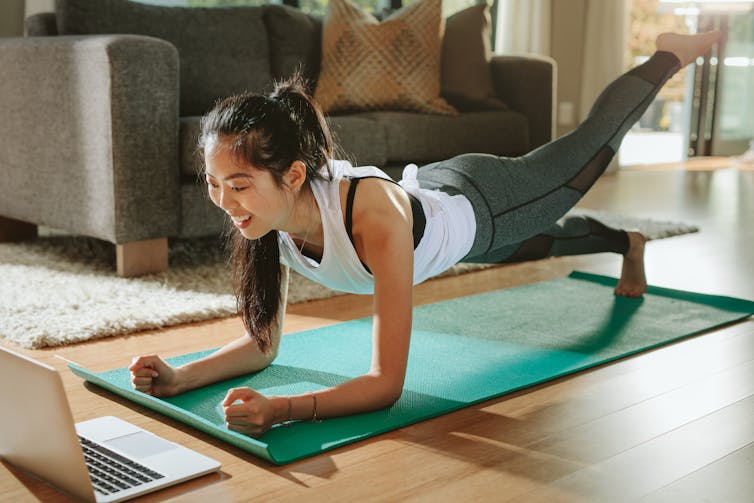 A woman doing planks with a leg outstretched and looking at laptop.