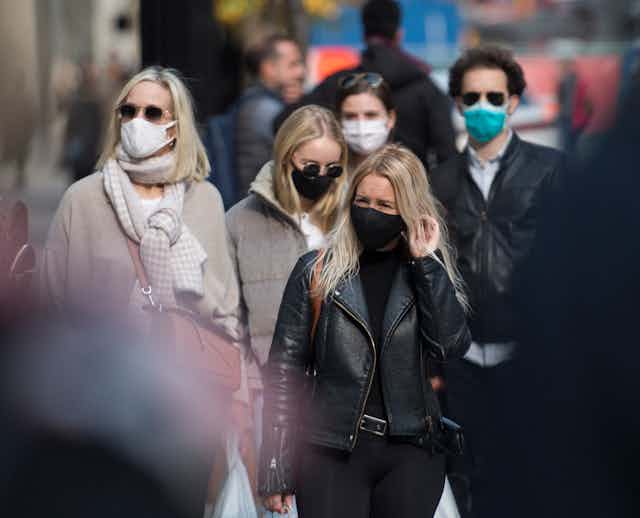 People in winter clothing wearing face masks walking down the street.