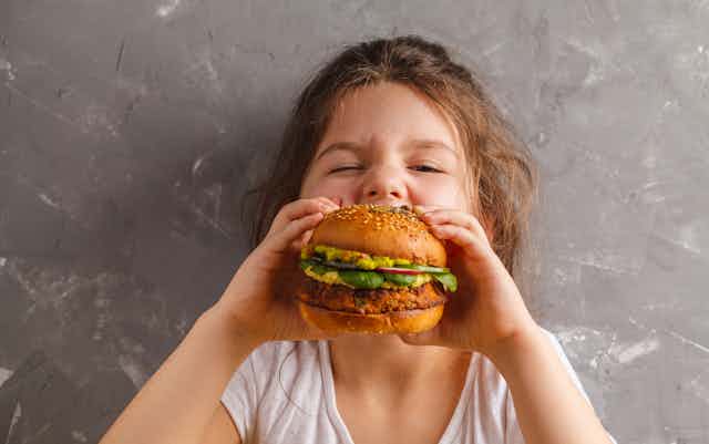 A young girl biting into a veggie burger.
