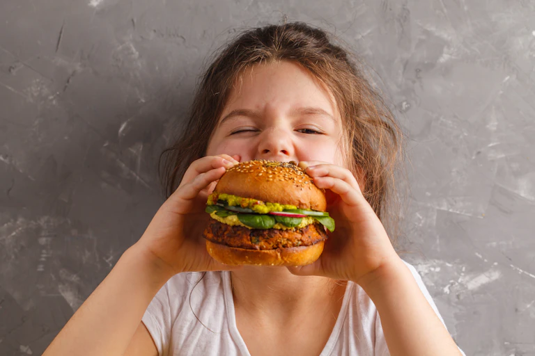 A young girl biting into a veggie burger.