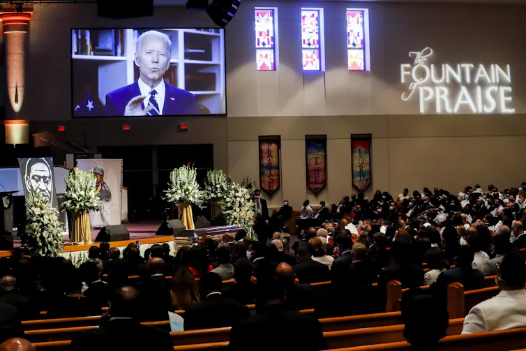 Video screen showing Joe Biden in church with pews of people.
