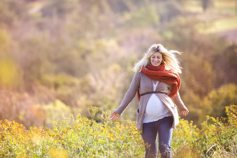 Pregnant women in scraf and cardigan walking through field.