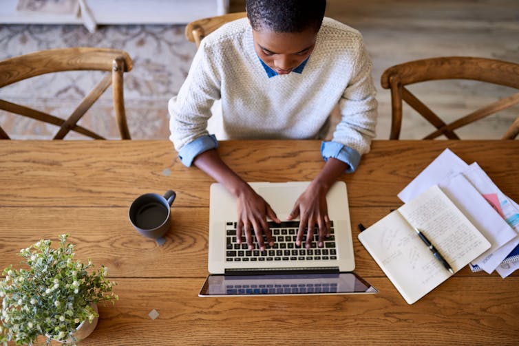 An overhead shot of a woman typing on a laptop at a table.