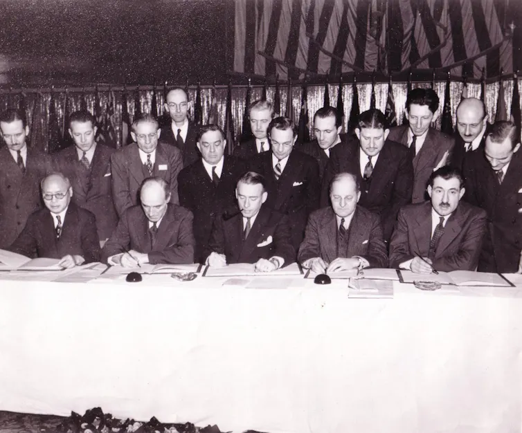 A black-and-white photograph of men standing around a table.