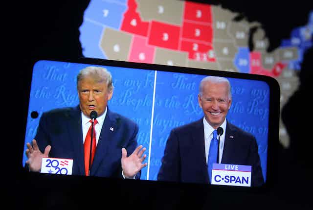 Debate electoral entre Trump y Biden visto en un teléfono móvil, con mapa de Estados Unidos detrás.