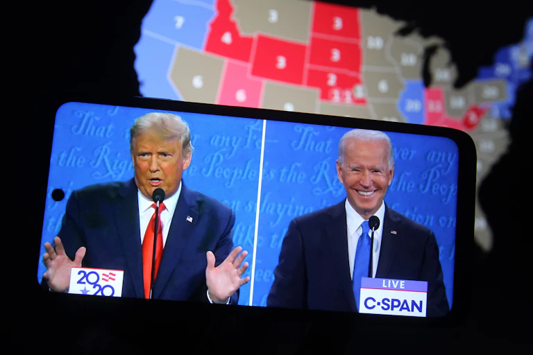 Debate electoral entre Trump y Biden visto en un teléfono móvil, con mapa de Estados Unidos detrás.