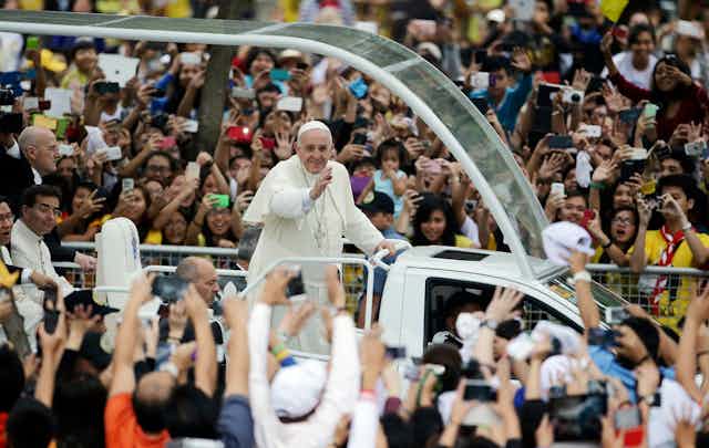 The Pope waves at people in a crowd.