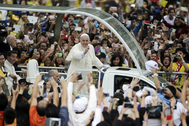The Pope waves at people in a crowd.