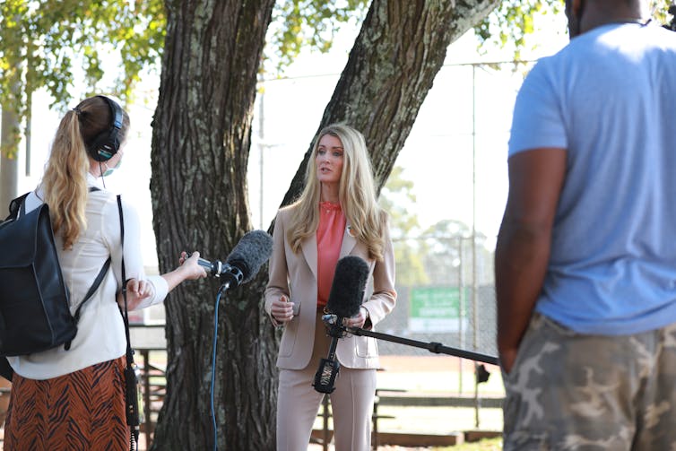 Loeffler speaks in front of a tree, wearing a beige pantsuit