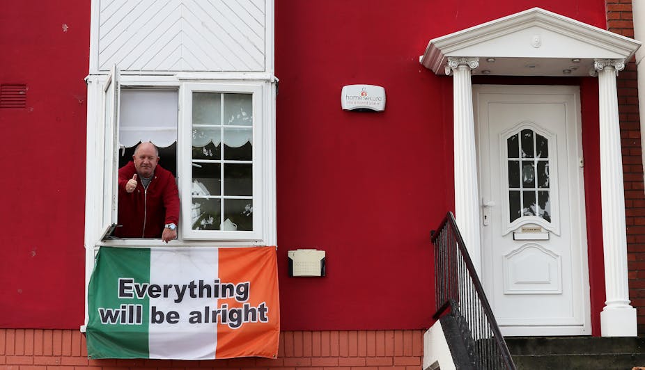 A man leans out a house window above an Irish flag that says "everything will be alright"