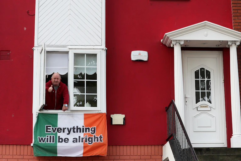 A man leans out a house window above an Irish flag that says "everything will be alright"