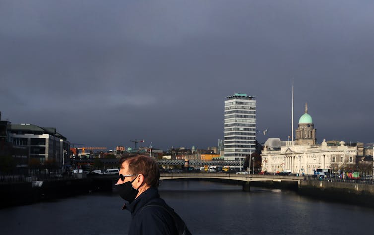 A man wearing a mask walks across a bridge in Dublin.