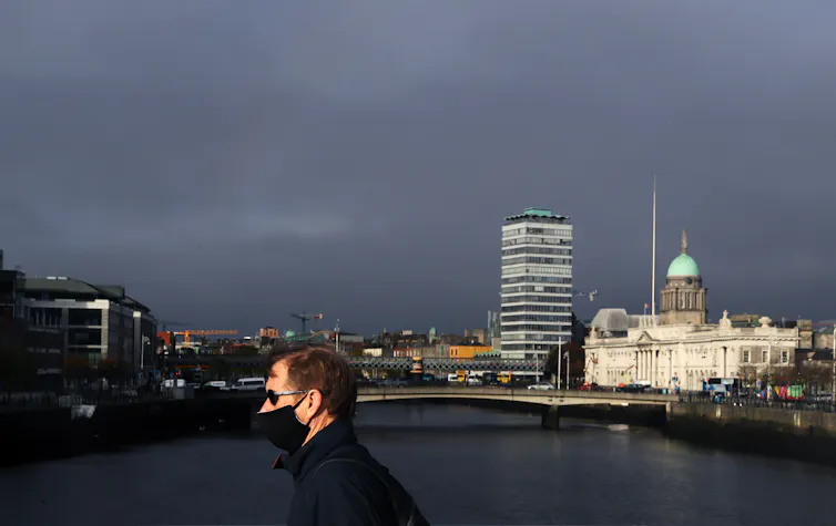 A man wearing a mask walks across a bridge in Dublin.