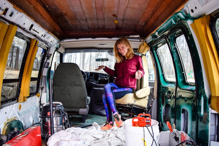A woman sits smiling in the back of her van.