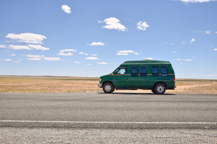 A green van is seen on a sunny, deserted highway.