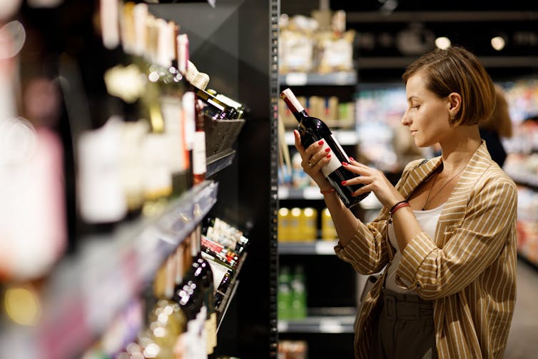 A woman looks at a bottle of wine in a store.