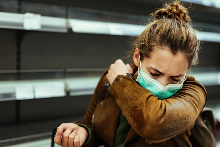 A woman coughs into her elbow.