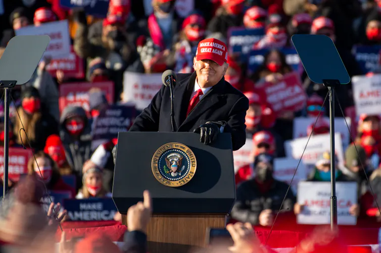 Donald Trump in front of a podium with supporters behind.