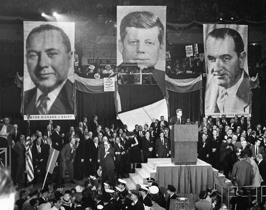 Presidential candidate John F. Kennedy speaks before a throng of supporters in front of banners depicting the faces of Kennedy, Chicago mayor Richard Daley and vice presidential candidate Lyndon B. Johnson.