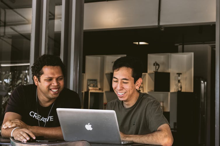 Two men sit looking at a laptop.