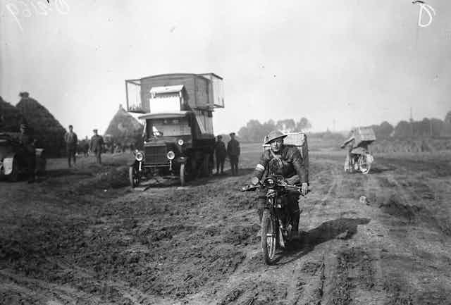 A man on bicycle watched by still soldiers.