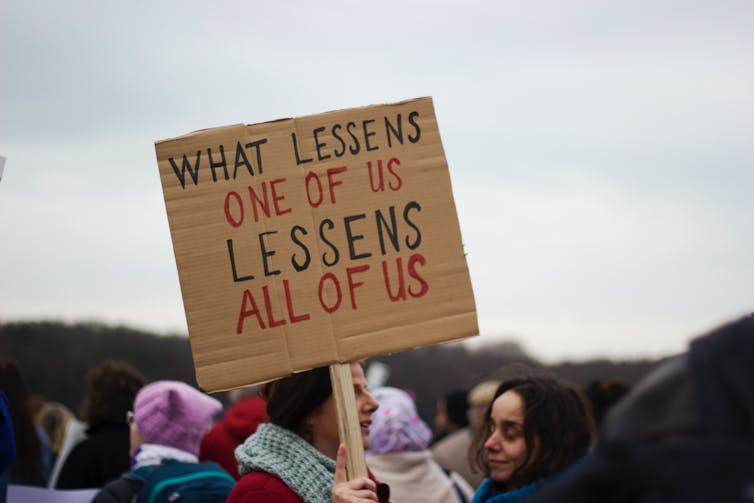 Protest sign reads: What lessens one of us lessens all of us