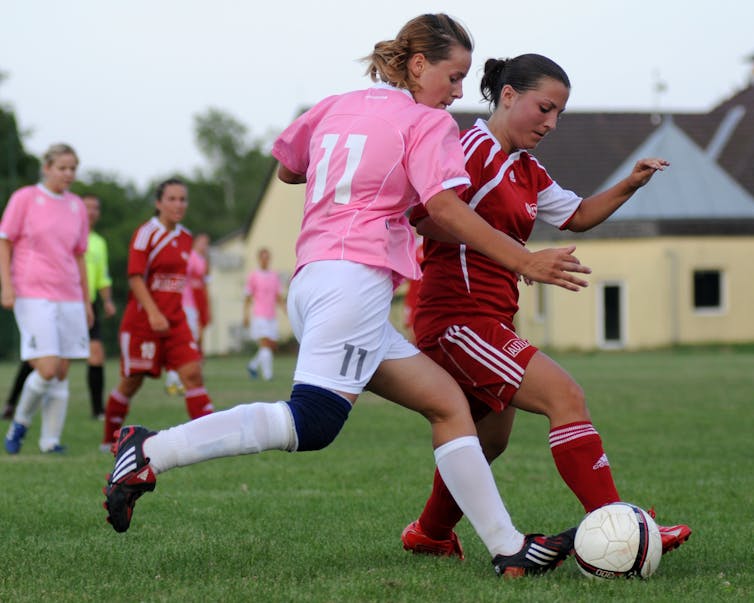 Teenage girls playing soccer outside, both trying to kick the ball.