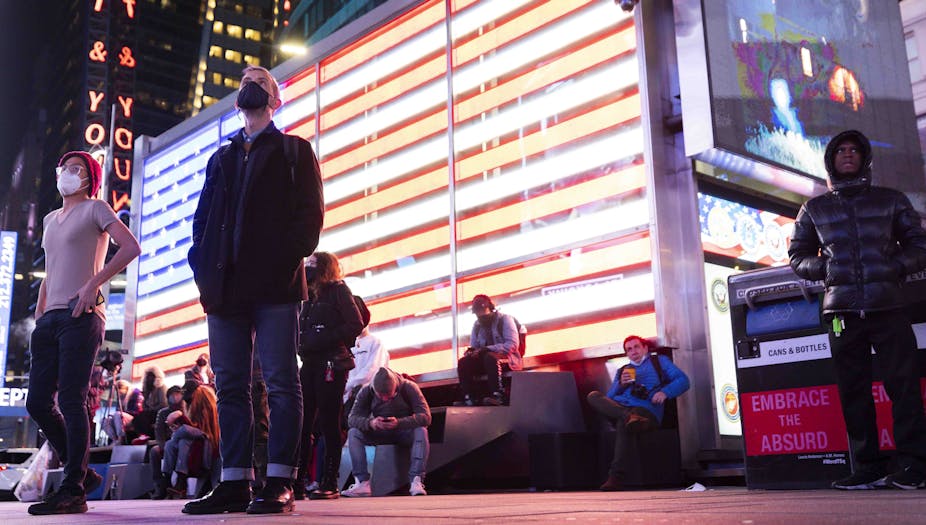 People standing looking upwards with an illuminated American flag behind. 