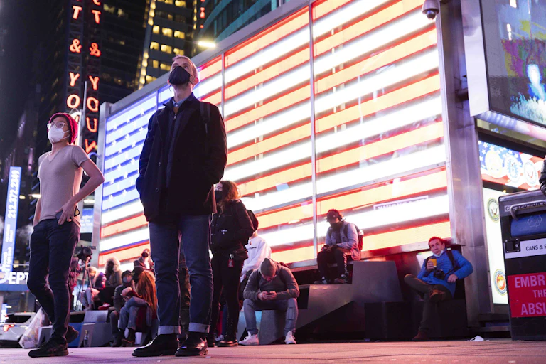 People standing looking upwards with an illuminated American flag behind.