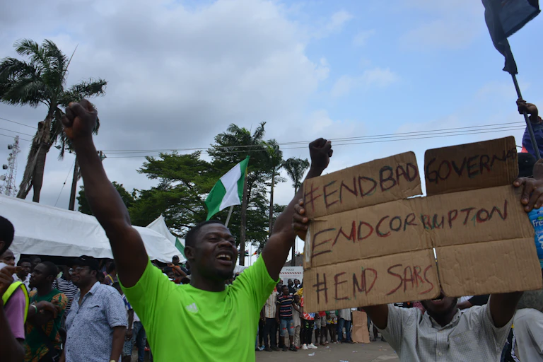 A man raises his arms and another holds a poster while a crowd stands outdoors