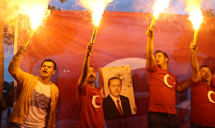 Men holding torches hold poster of Turkish president Recip Tayyip Erdoğan