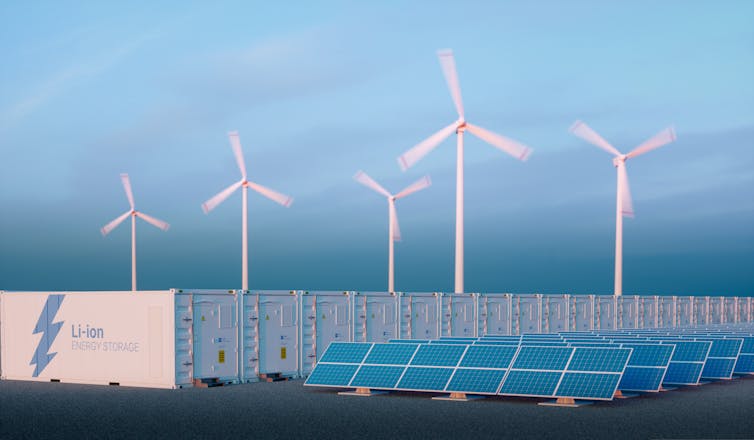 A row of wind turbines in the background with solar panels and large battery modules in the foreground.